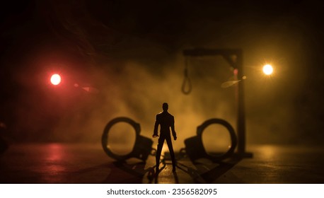 Legal law or crime and execution concept. Death penalty miniatures on table. Man alone looking to execution at night. Artwork decoration with handcuffs, Statue of Justice and mallet of justice