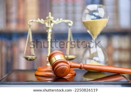 Legal office of lawyers, justice and law concept : Judge's gavel or hammer and base used by a judge person on a desk in a courtroom with blurred weight scale of justice, bookshelf, hourglass behind.