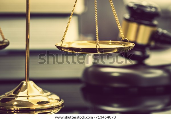 Legal office of lawyers, justice and law concept :\
Brass scales of justice with blurred wooden judge gavel or wood\
hammer and a soundboard on  judiciary desk in a courtroom with\
thick law books behind