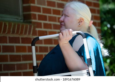 Legally Blind Woman Carrying A Step Stool To The Exterior Wall Of Her Home So That She Can Do Home Repairs