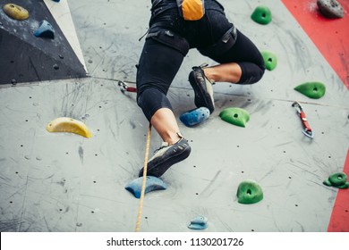 Leggs of sportswoman rock climber. Rock climber moving up on a rocky artificial wall. Legs and climbing shoes close up. - Powered by Shutterstock