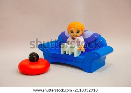 Lego girl sits on a blue sofa, next to a red stand with a black ball