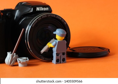 Lego Mini Figure Of Man In Janitor Uniform Cleaning Lense On Camera. Editorial Image, Close Up Photo Isolated On Orange Background, Macro Photography, Concept Of People Doing Their Job. 