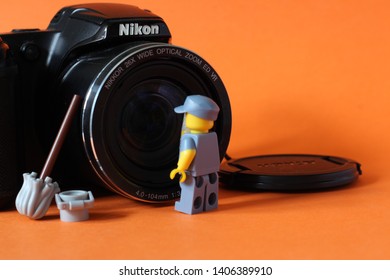 Lego Mini Figure Of Man In Janitor Uniform Cleaning Lense On Photo Camera With Bucket And Mop Next To Him. Editorial Image, Close Up Photo Isolated On Orange Background, Macro Photography, Close Up. 