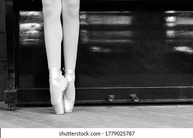Legs of a ballerina in pointe shoes against the background of an old piano. Close-up. Black and white photo. Classical dances. Training.