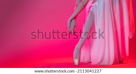 Legs of a ballerina in pointe shoes stand on a pink background