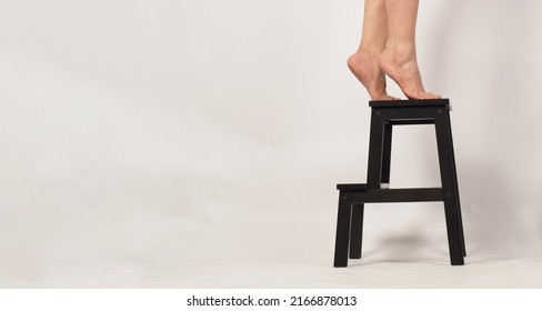 Legs and Barefoot stand on tiptoe on a step stool or wooden stairs with white background. Side view.