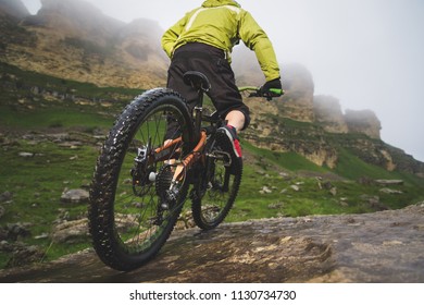 Legs of bicyclist and rear wheel close-up view of back mtb bike in mountains against background of rocks in foggy weather. The concept of extreme sports