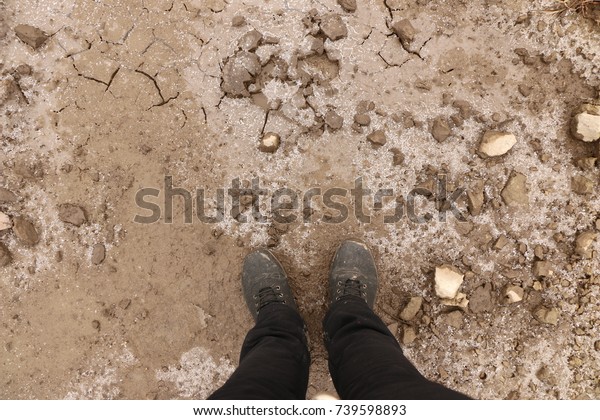 legs\
in black pants and boots on dirt and ice with\
cracks