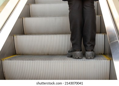 Legs in black pants on step of escalator in shopping mall. Metal staircase. Up escalator. Close-up.