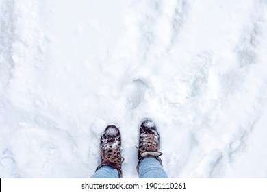 Legs in burgundy boots and blue jeans in the snow. Footprints in the snow. Winter landscape. Soft focus. Top view