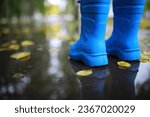 legs of child in blue rubber boots jumping in autumn puddles