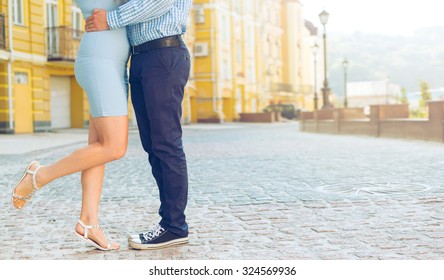Legs close up. Fashion summer of hipster couple. Close up of feet. Man and woman posing on the city street. Blue dress woman. Man's sneakers and denim. Woman standing on tiptoe try to kiss man. Love.