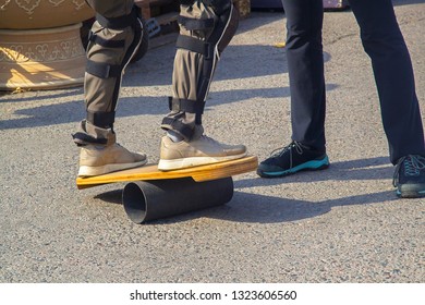 Legs of coach & person with protective knee-pads standing on balance board