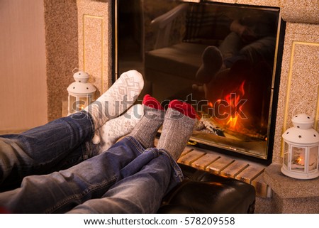 Legs of couple in woolen socks heat up near cozy fireplace, warm toned image