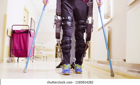 Legs of disable man in the robotic exoskeleton walking through the corridor of the rehabilitation clinic. Doctor helping him.