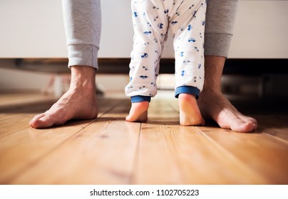Legs of father and a toddler boy standing on the floor in bedroom at home.
