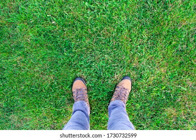 Legs And Feet Standing On Grass. A Man Wearing Light Jeans And Brown Boots Is Standing In A Field Of Beautiful Green Grass. Image Is Looking Down, In A POV (point Of View) Angle. Copy Space Available.