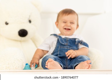 Legs In Focus, Happy Little Baby Six Months Old In Blue Jeans Sits Next To A Large Teddy Bear