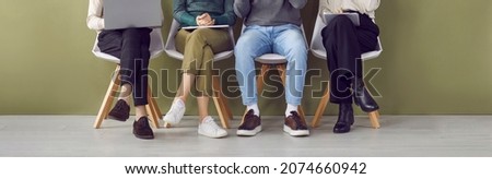 Legs of four job applicants sitting on chairs in hallway waiting in line for interview. Unknown candidates for jobs in casual clothes and shoes are sitting with documents and gadgets. Hiring concept.