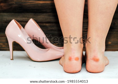 Legs of a girl with calluses in fashionable pink high-heeled shoes with a pointed toe on a wooden background.