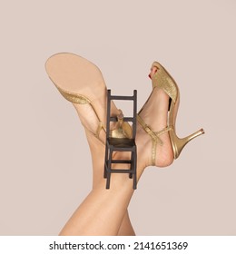 Legs of a girl in dancing shoes with a hanging model of a chair hanging on a heel. A metaphor for rest and a dance floor.