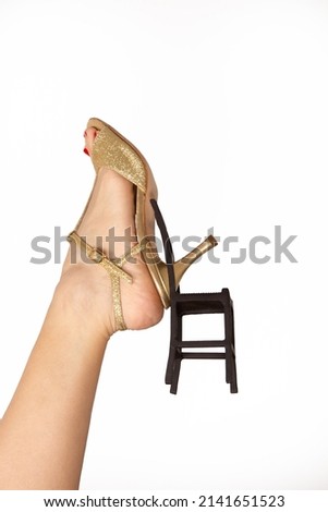 Legs of a girl in dancing shoes with a hanging model of a chair hanging on a heel on a white background. A metaphor for rest and a dance floor.
