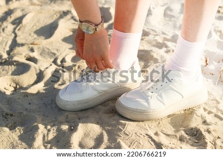 Legs of a girl in a skirt in fashionable sneakers on the sand, the image is taken for a walk.