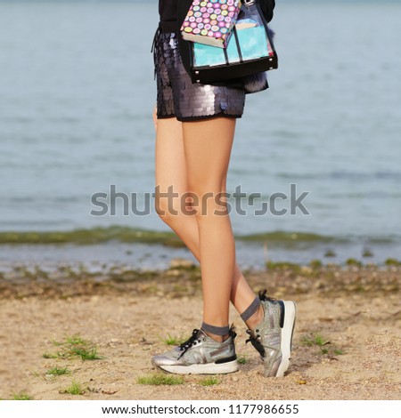 Legs of a girl in sneakers walking along the beach