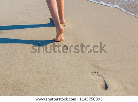 legs of a girl walking on a sandy beach along the water's edge
