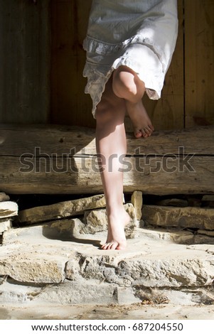 The legs of the girl in a white dress that stands with one foot on the cymbals on the old stone steps, and the second leg bent resting on the wooden beam