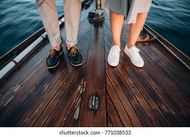 The legs of a guy and a girl in stylish shoes that stand on a wooden yacht floating on the sea