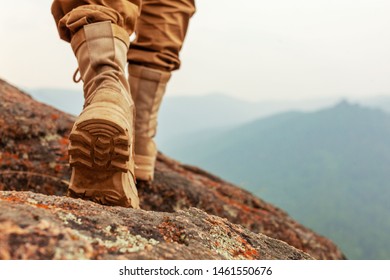 Legs In High Yellow Army Boots Walking On Stones, Concept Of Hiking And Adventure