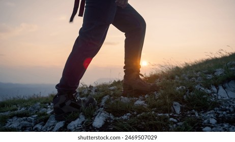 Legs in hiking boots walking on rocky grass terrain, the setting sun in the background. Hike, mountaineering, and trekking concepts. - Powered by Shutterstock