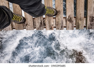 Legs In Hiking Shoes On The Edge Of A Wooden Bridge Over Stormy Water. Suicide Theme