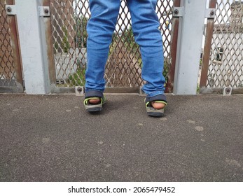 The Legs Of A Kid Standing By The Meshed Metal Door