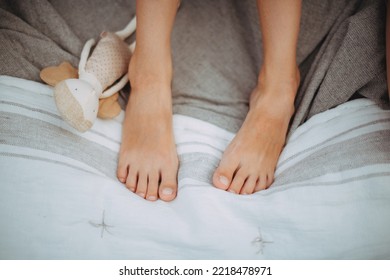 The Legs Of A Little Girl On A Blanket At A Picnic. Close-up. No Face Visible. A Small Rag Baby Doll On The Bedspread.