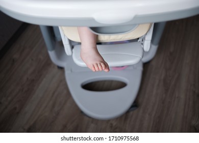 The Legs Of A Little Toddler Sitting In A High Chair At The Dining Table
