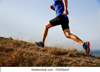 legs male athlete runner running uphill on trail background of sky