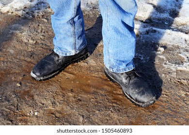 Legs Of A Man In Jeans And Army Boots Standing On Dirty Snowy Soil