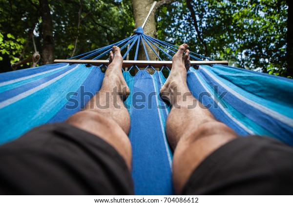 Legs of a man lying on a hammock in the woods.\
Illuminated from above.