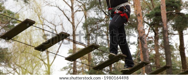 Legs of a\
man in sports equipment are walking on a suspension bridge bottom\
up view in European outdoor forest rope park at spring summer day -\
climbing sport active\
recreation