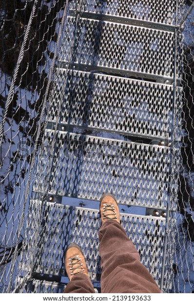 legs of man that walks on the very long \
suspension bridge in stainless steel in\
winter