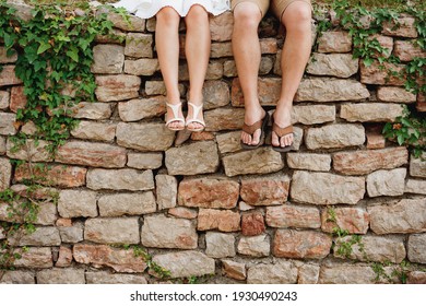 Legs of a man and a woman sitting side by side on the stone fence 