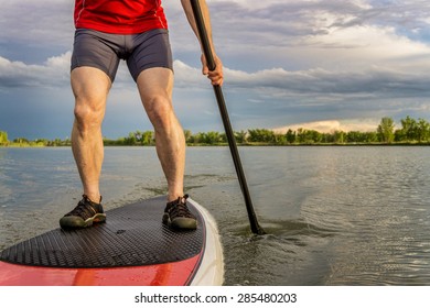 Legs Of Muscular Male Paddler On A Stand Up Paddleboard - A Calm Lake In Summer