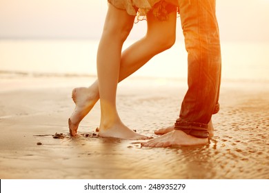 Legs on beach. Foot spa. A young  loving  couple hugging and kissing on the beach at sunset. Two lovers, man and woman barefoot near the water. Summer in love 