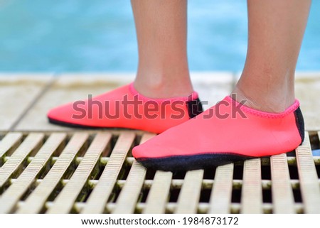 Legs with pink swimming footwear.Young girl's feet wearing swim shoes by the pool.
