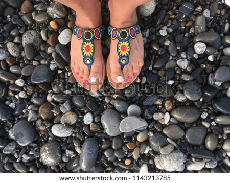 Legs in sandals with an ethnic pattern on the background of a pebble beach. Summer, sea, rest.
