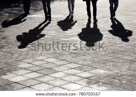 Legs and shadow of five young person approaching on city street pedestrian sidewalk