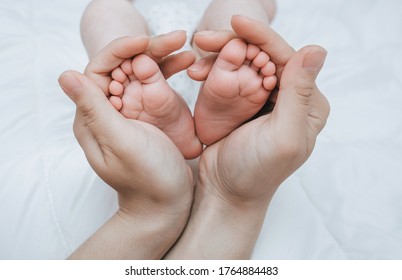 Die Beine eines kleinen Kindes, das auf einem weißen Bett in den Armen seiner geliebten Mutter schlafen, Nahaufnahme. Frau ist glücklich. 